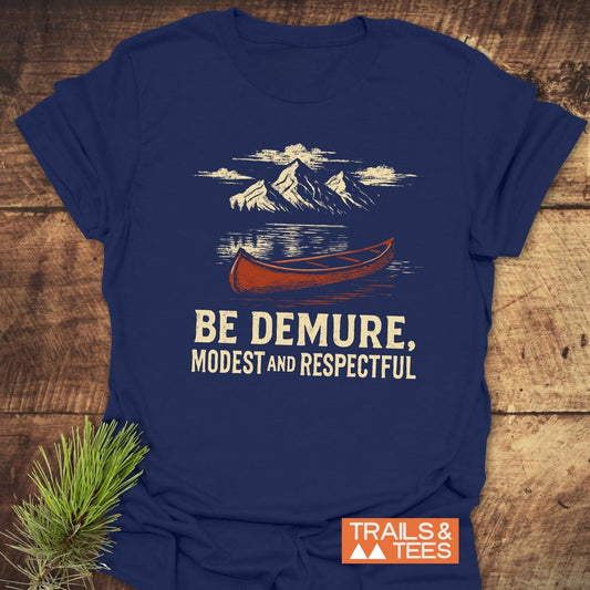 Be Demure Canoe T-Shirt featuring snow-capped mountains and canoe graphic, on navy-blue, crafted from soft cotton for comfort and durability, by Trails & Tees.