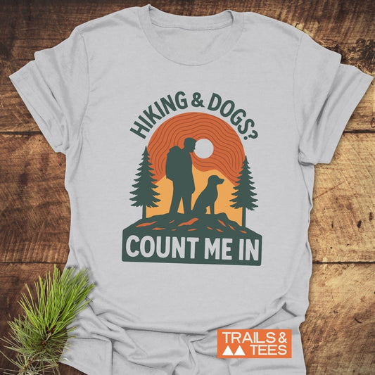 Hiking And Dogs T-Shirt featuring a graphic of a hiker and dog with pine trees and an orange backdrop, emphasizing outdoor adventure and comfort.