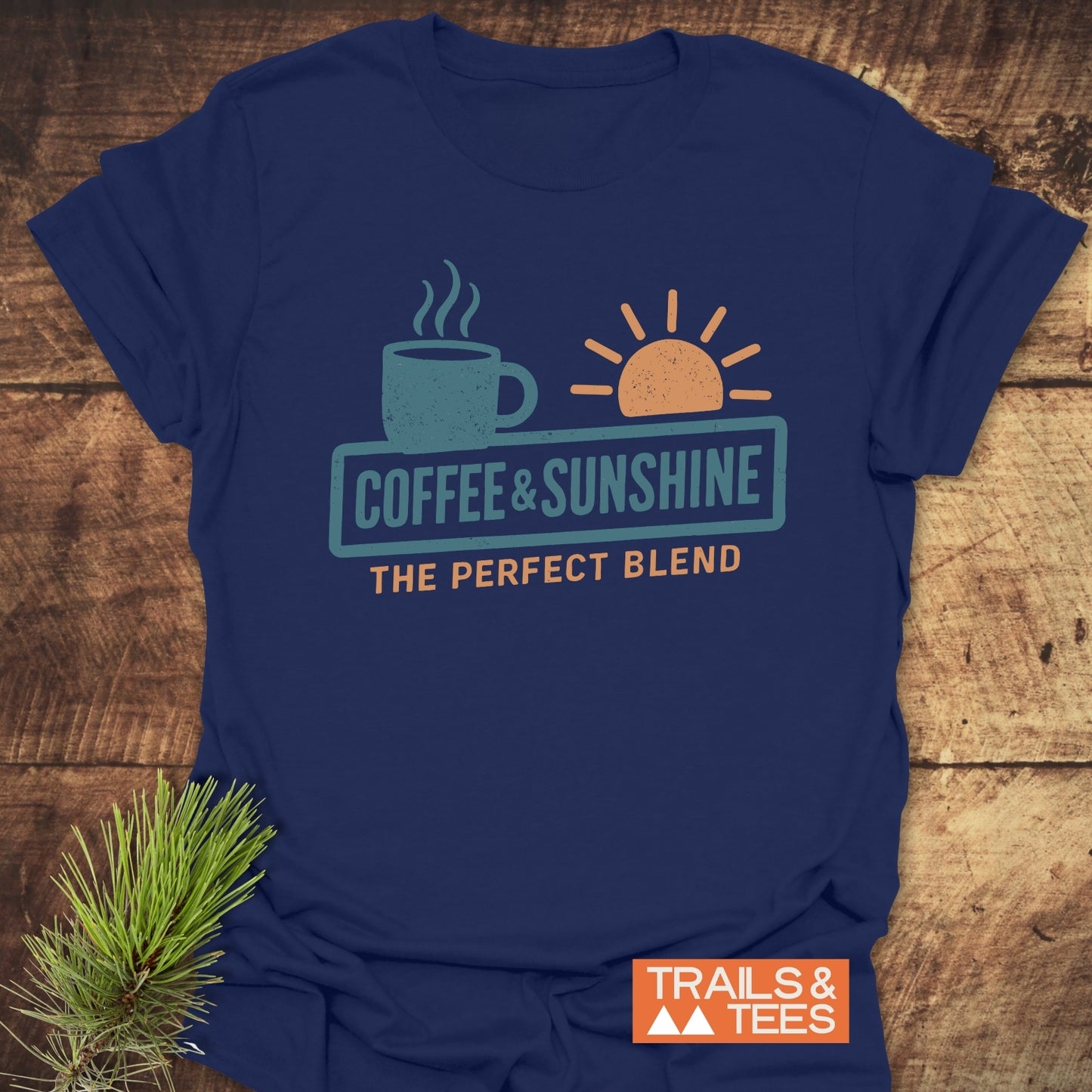 Coffee & Sunshine T-Shirt with steaming mug and sun design, showcasing soft ring-spun cotton on a rustic wood surface, highlighting outdoor adventure spirit.