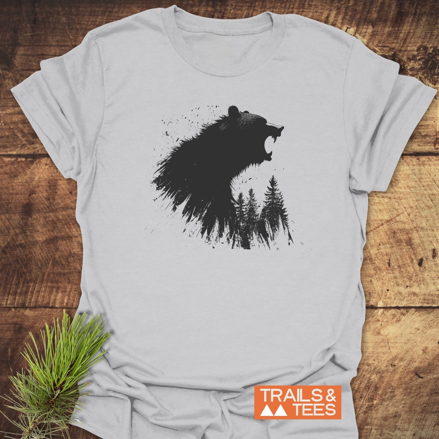 Roaring Bear Forest T-Shirt on wooden surface, featuring a bear profile with pine trees graphic, TRAILS & TEES logo, emphasizing outdoor comfort and durability.