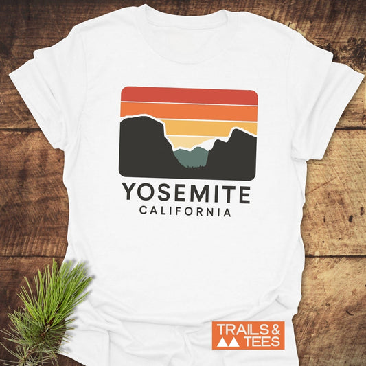 Retro Yosemite T-Shirt featuring a sunset-striped sky and mountain graphic, crafted from soft ring-spun cotton. Includes a small TRAILS & TEES logo.