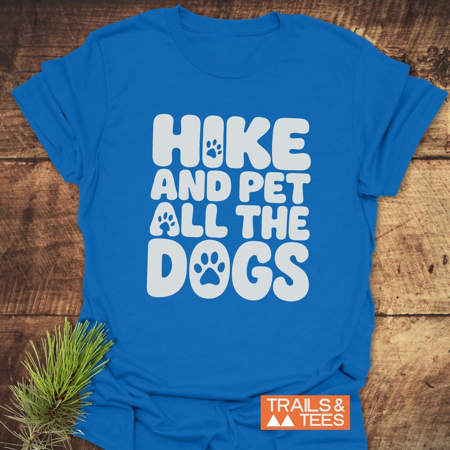 Hike And Pet Dogs T-Shirt, bright blue with a playful slogan in white bubbly letters, showcased on wood. Features durable, soft cotton, ideal for adventure lovers.