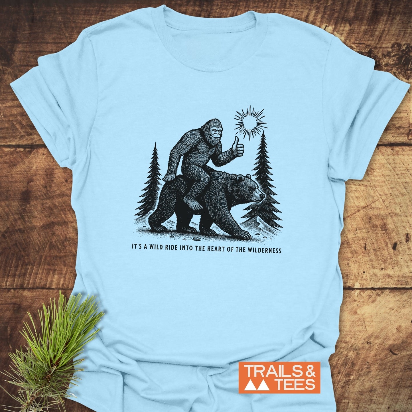 Wild Ride Bigfoot T-Shirt featuring Sasquatch on a bear with a sunburst. Made from soft ring-spun cotton, pre-shrunk, durable design for outdoor enthusiasts.