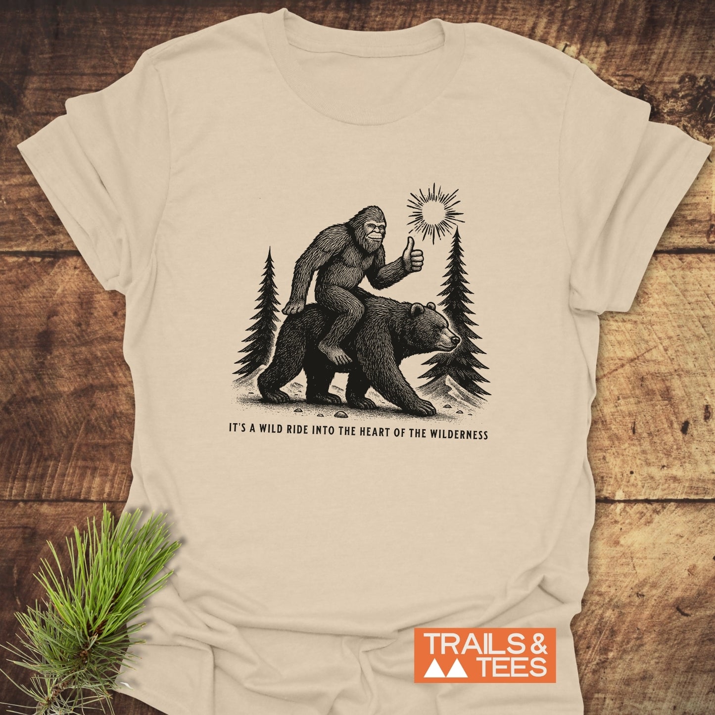 Wild Ride Bigfoot T-Shirt featuring Sasquatch on a bear through forest scene, slogan beneath. Made from soft, durable cotton for outdoor adventures.