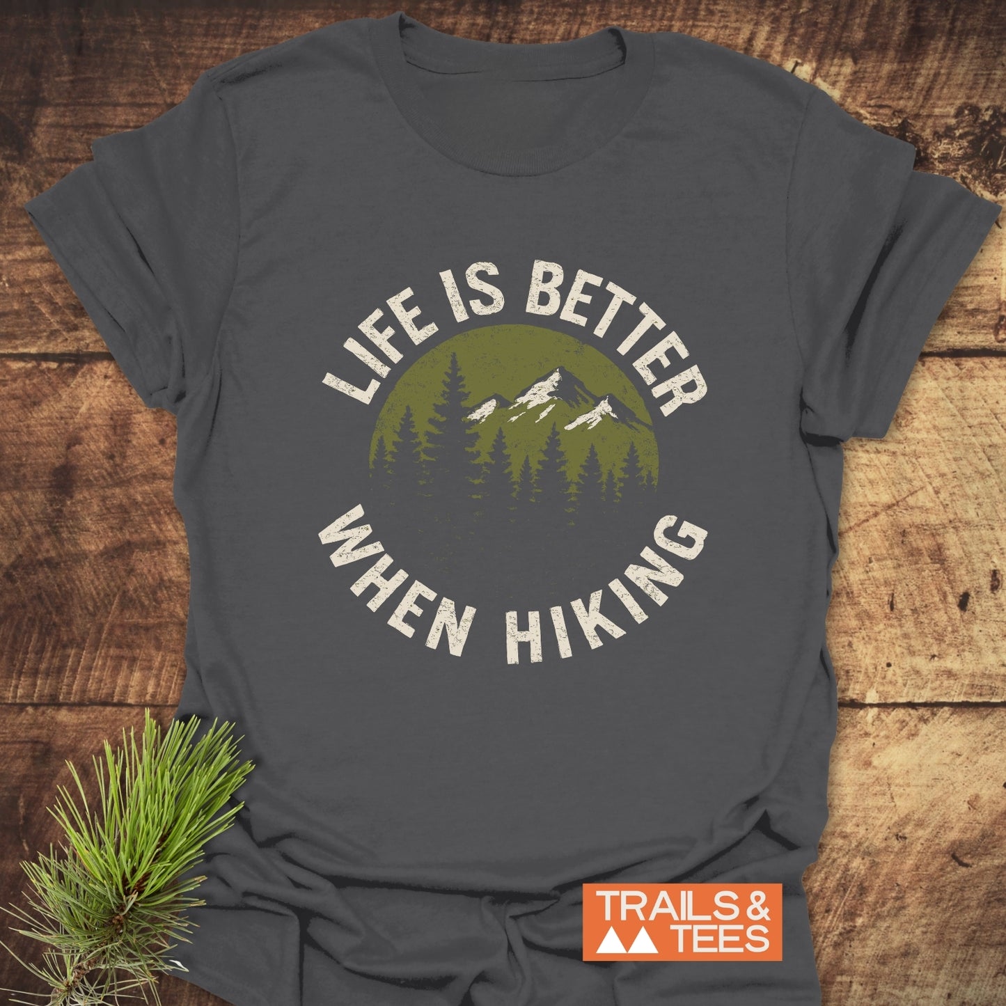 Life Is Better When Hiking T-Shirt featuring a mountain and pine tree design on gray fabric, highlighting outdoor adventure and comfort.