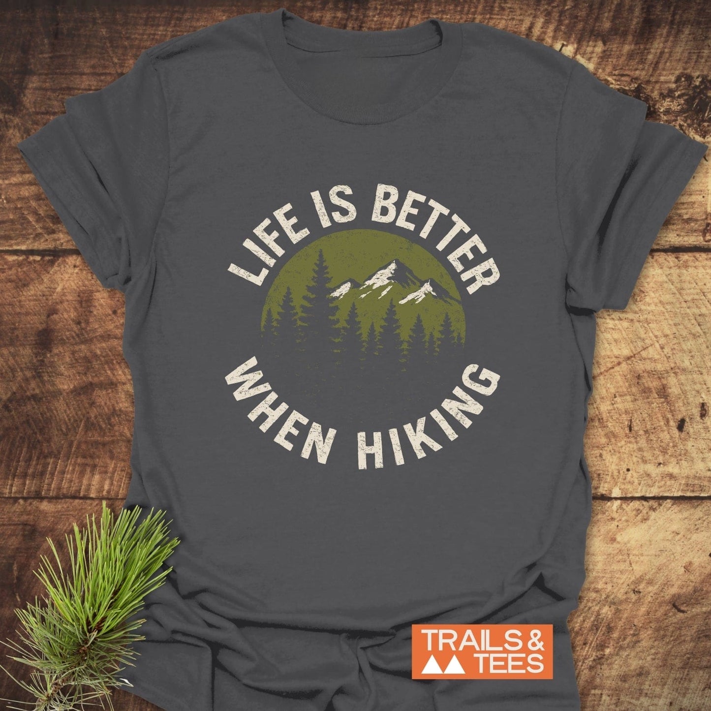 Life Is Better When Hiking T-Shirt featuring a mountain and pine tree design on gray fabric, highlighting outdoor adventure and comfort.