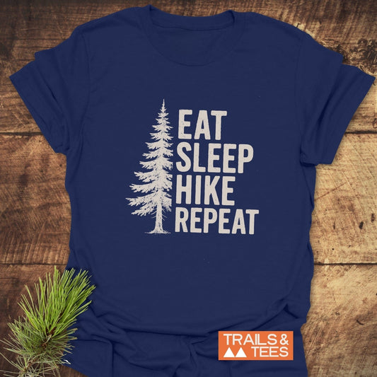Hike, Repeat T-Shirt featuring a white pine tree graphic and text on navy-blue, with a Trails & Tees logo; styled with pine sprigs.