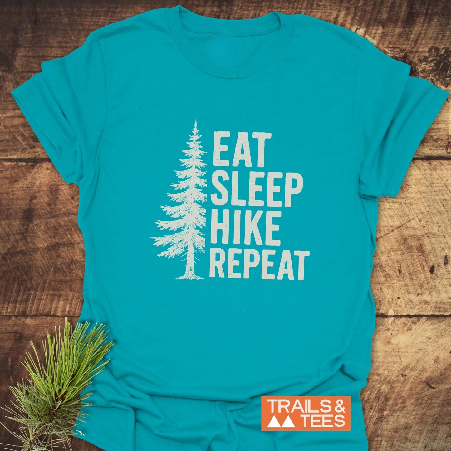 Hike, Repeat T-Shirt featuring a white pine tree graphic and slogan, “EAT SLEEP HIKE REPEAT,” on soft, ring-spun cotton. Ideal for outdoor enthusiasts.