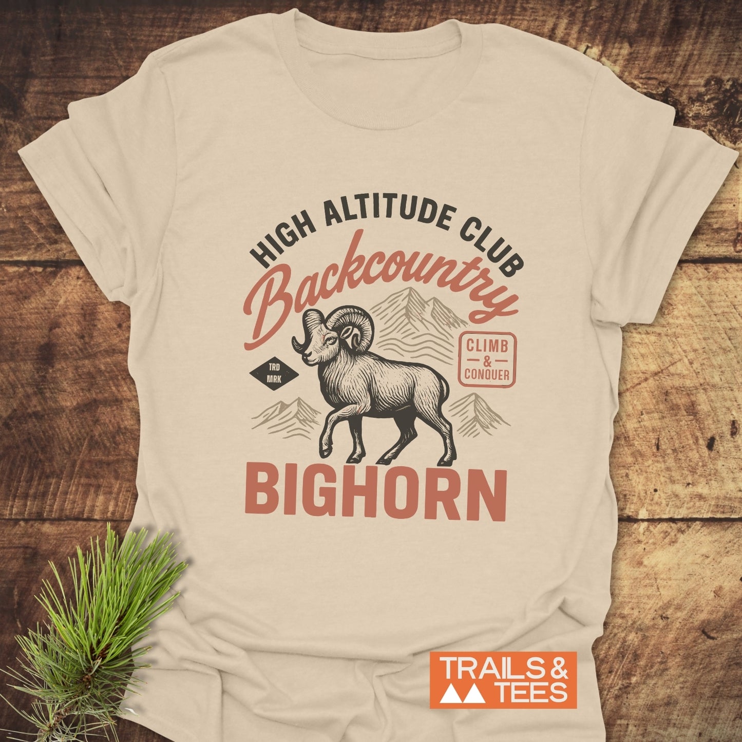 High Altitude Club T-Shirt featuring a ram graphic, mountain outlines, and text details, laid on wood. Lightweight, durable, and pre-shrunk for comfort.
