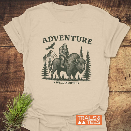 Bigfoot & Bison T-Shirt featuring a vintage-style illustration of Bigfoot on a bison, with pine trees and mountains, embodying outdoor adventure by Trails & Tees.