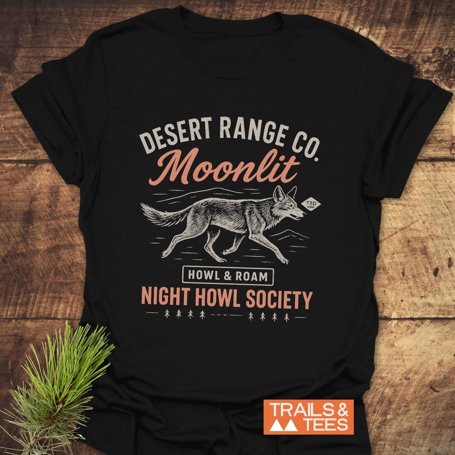 Night Howl Society T-Shirt featuring a vintage graphic of a coyote and text, laid on wood, evoking an outdoorsy, desert-meets-nighttime vibe.