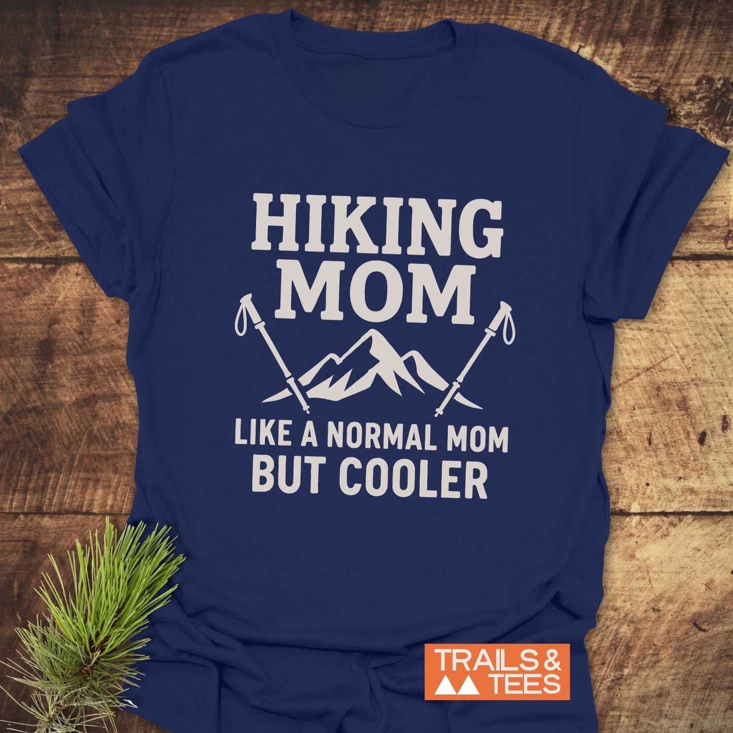 Navy-blue Hiking Mom T-shirt with mountain and hiking pole design, emphasizing comfort and durability, styled with pine branch and TRAILS & TEES logo.