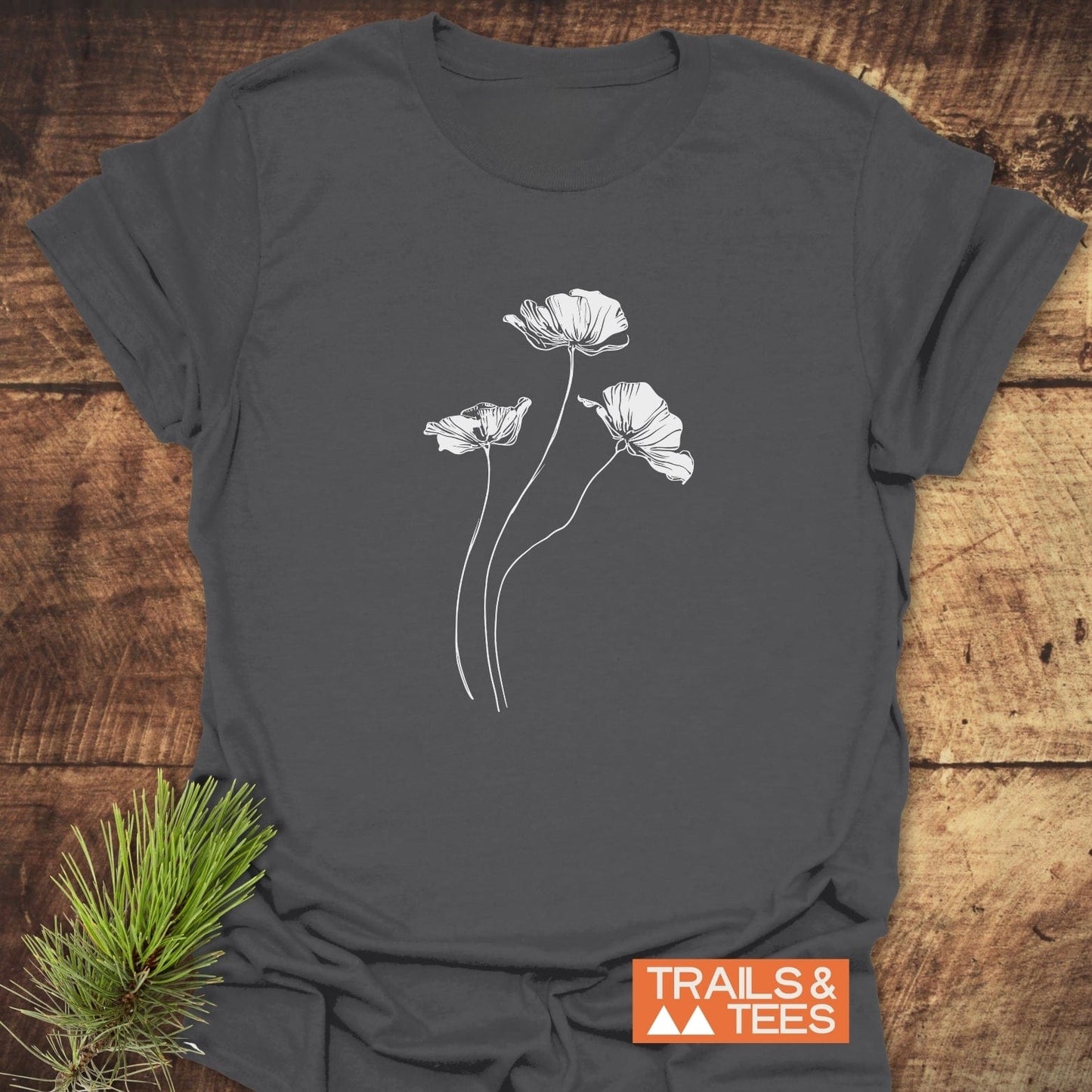 Delicate Poppies T-Shirt: Charcoal-gray tee with white poppy line-drawing, showcasing outdoor-inspired style and comfort, alongside TRAILS & TEES logo and pine sprig accent.