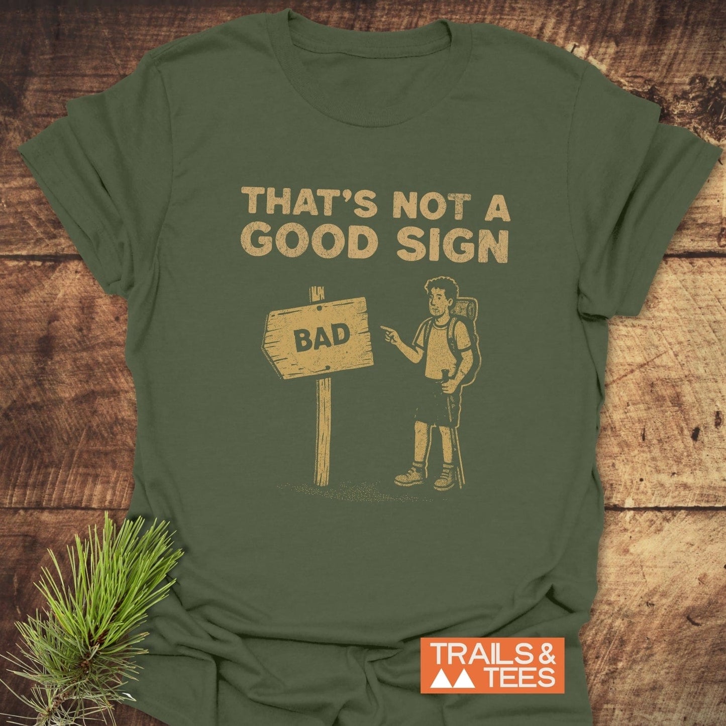 Bad Sign Funny T-Shirt with a hiking cartoon on an olive-green background, showcasing humor and outdoor spirit, made from soft, durable ring-spun cotton.