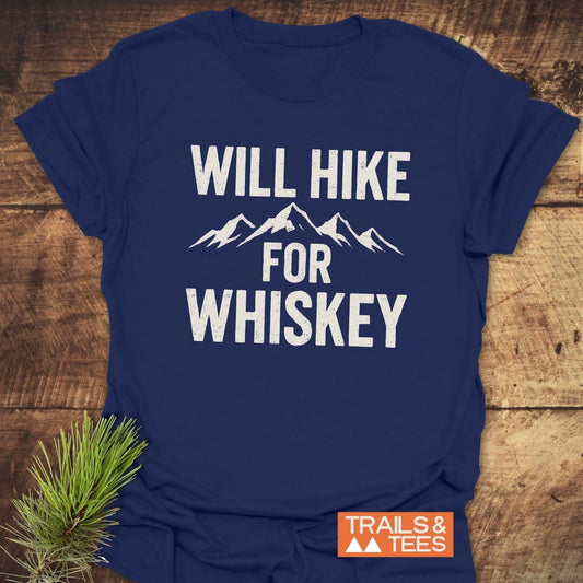 Will Hike For Whiskey T-Shirt with mountain graphic, laid on wood. Features distressed print, taped shoulders, durable, soft ring-spun cotton for outdoor adventures.