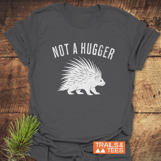 Not A Hugger T-Shirt with distressed porcupine graphic, emphasizing outdoor adventure. Laid on wood, featuring Trails & Tees logo, highlighting comfort and durability.