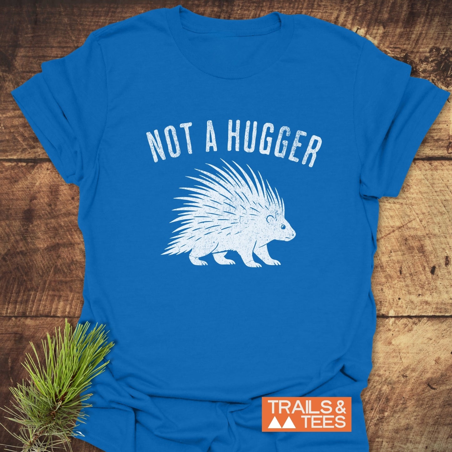 Not A Hugger T-Shirt displayed on wood, featuring a porcupine graphic and distressed lettering, embodying outdoor adventure with durable, comfortable design.