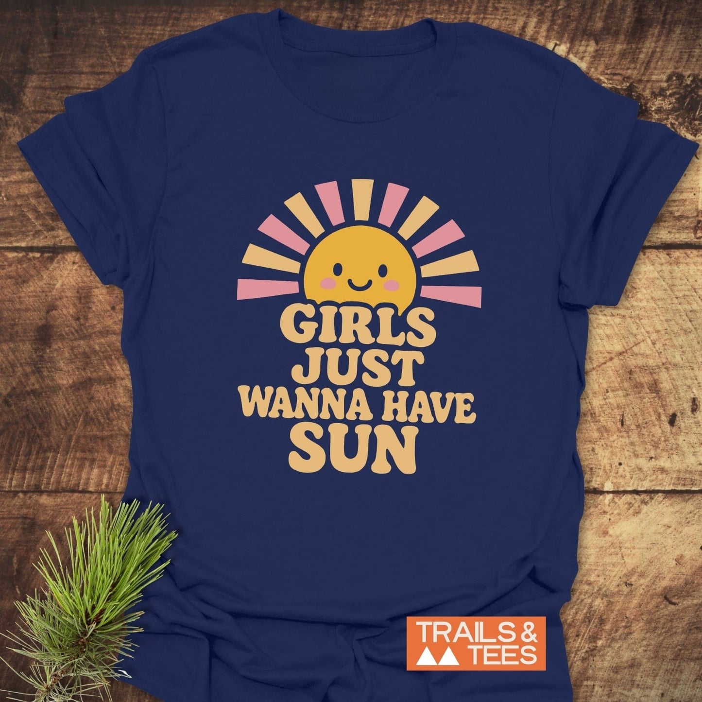 Girls Want Fun T-Shirt with a smiling sun and retro text, laid on wood. Made from soft, durable cotton by Trails & Tees.