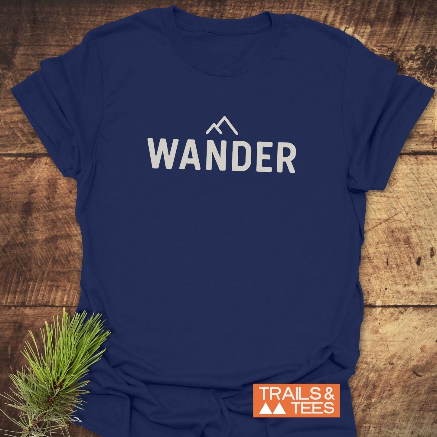 Navy blue 547 Wander Minimalist T-Shirt with WANDER text and mountain design; includes orange TRAILS & TEES label and spruce twig accent.