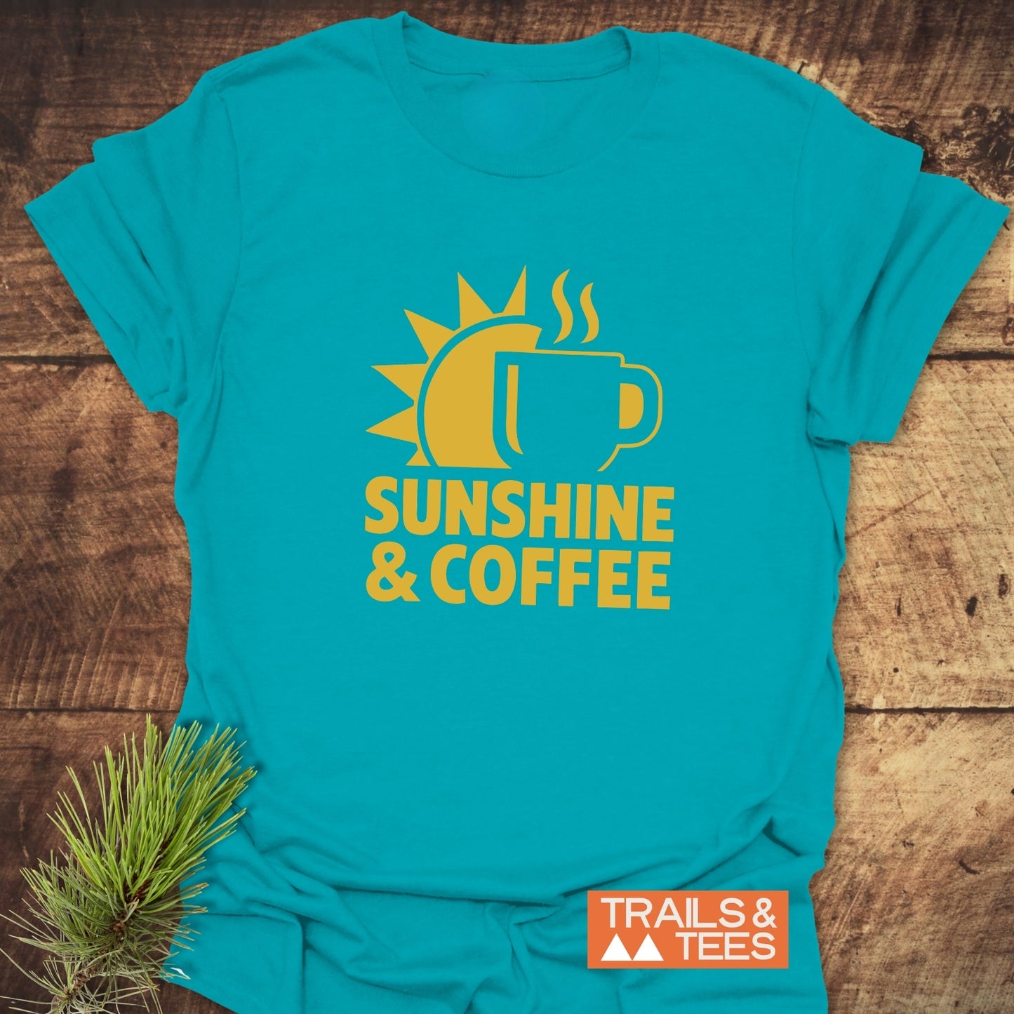 Bold Sunshine & Coffee T-Shirt featuring a rising sun and coffee mug graphic, showcasing outdoor-inspired comfort and style on a rustic wooden backdrop.
