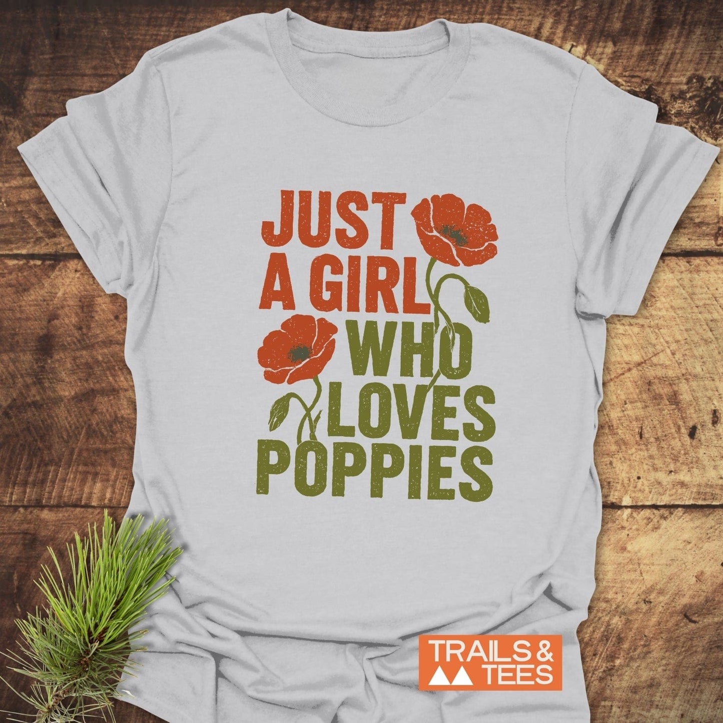 Grunge Poppy Love T-Shirt featuring poppy graphics and text, laid flat on wood. Made from soft cotton, combines durability with outdoor-inspired design.