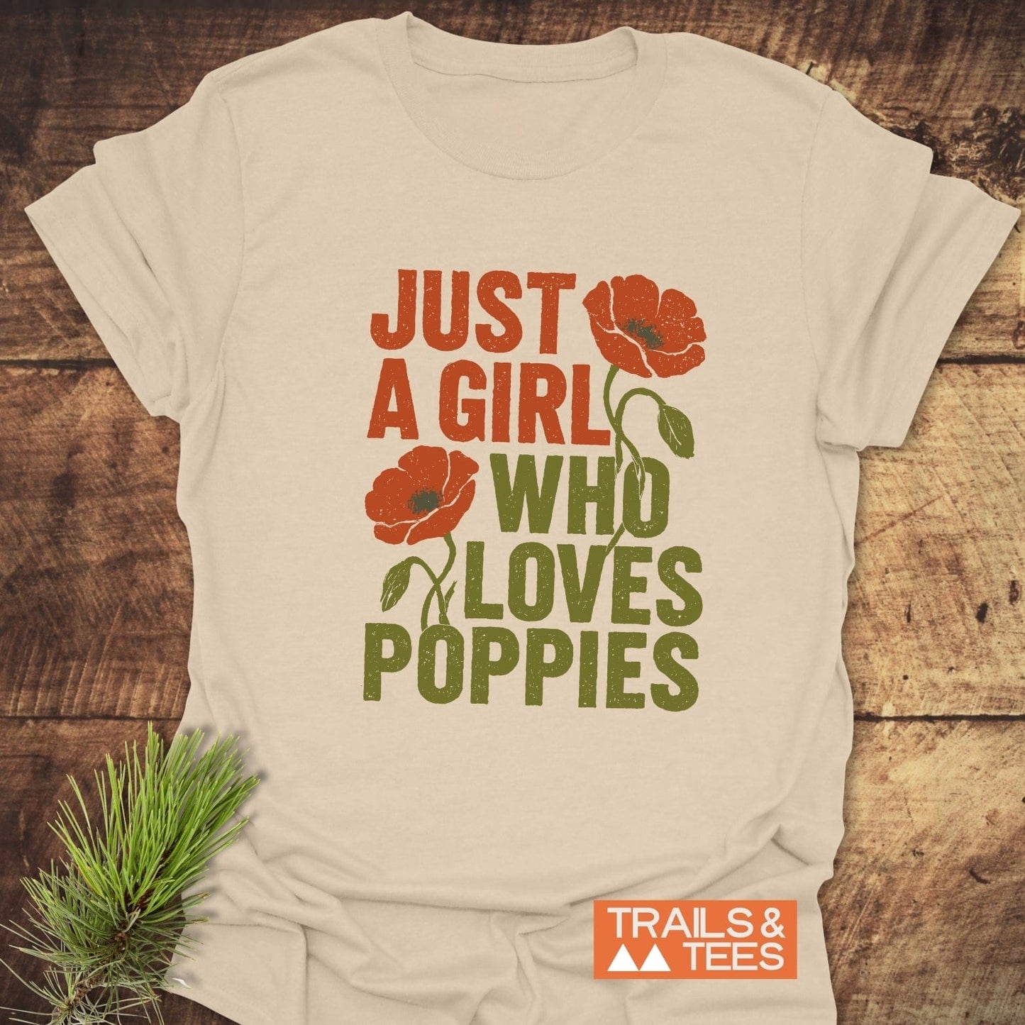 Grunge Poppy Love T-Shirt with orange poppy graphic and slogan, laid on wood, next to pine sprig; features durable, soft ring-spun cotton, pre-shrunk for fit.
