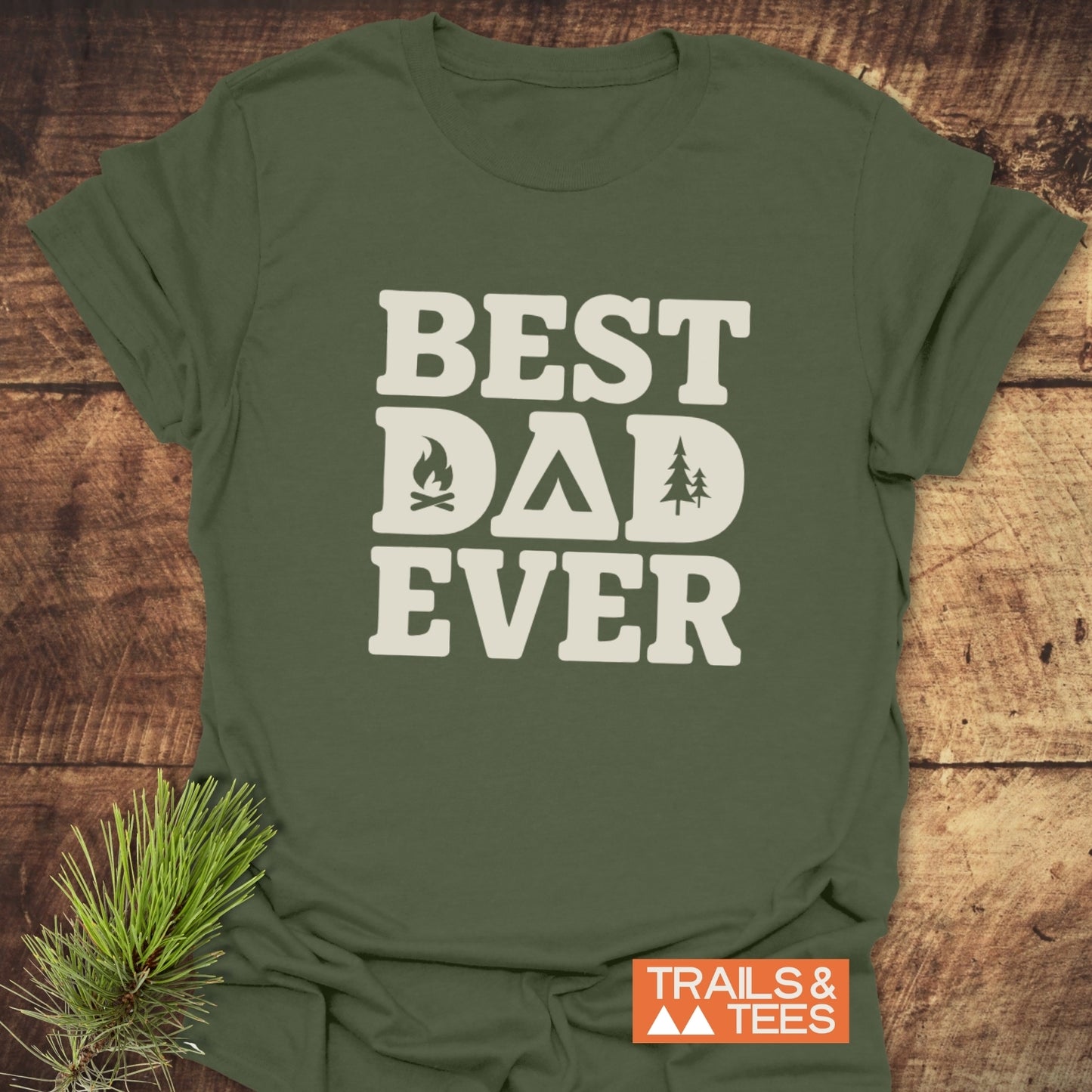 Olive-green 'Best Dad Ever' camping T-shirt with camping icons, laid on wood. Features durable, lightweight cotton, perfect for outdoor adventures.