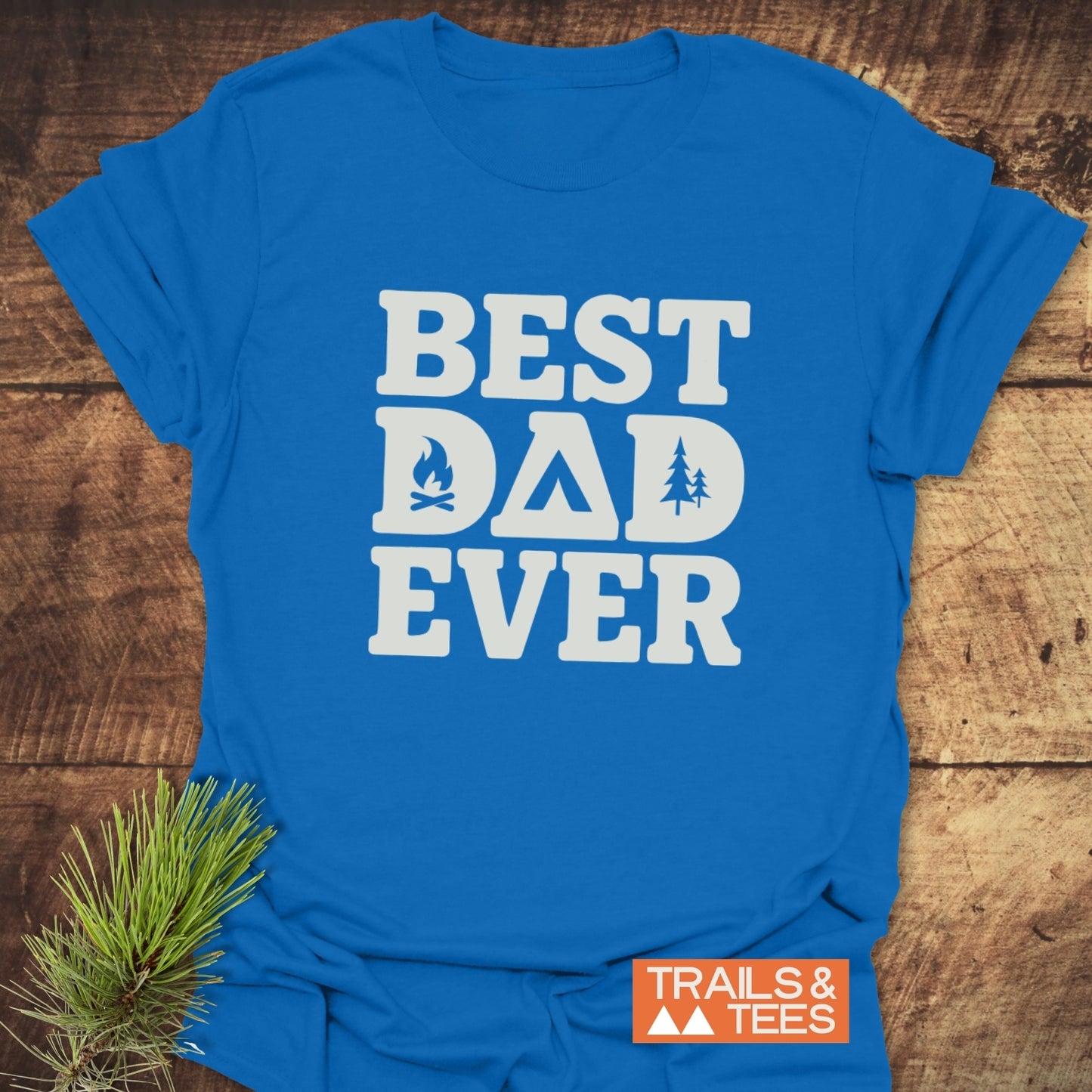 Royal-blue Best Dad Ever camping T-shirt, featuring outdoor icons, on a wooden background. Made from soft, ring-spun cotton for comfort and durability.