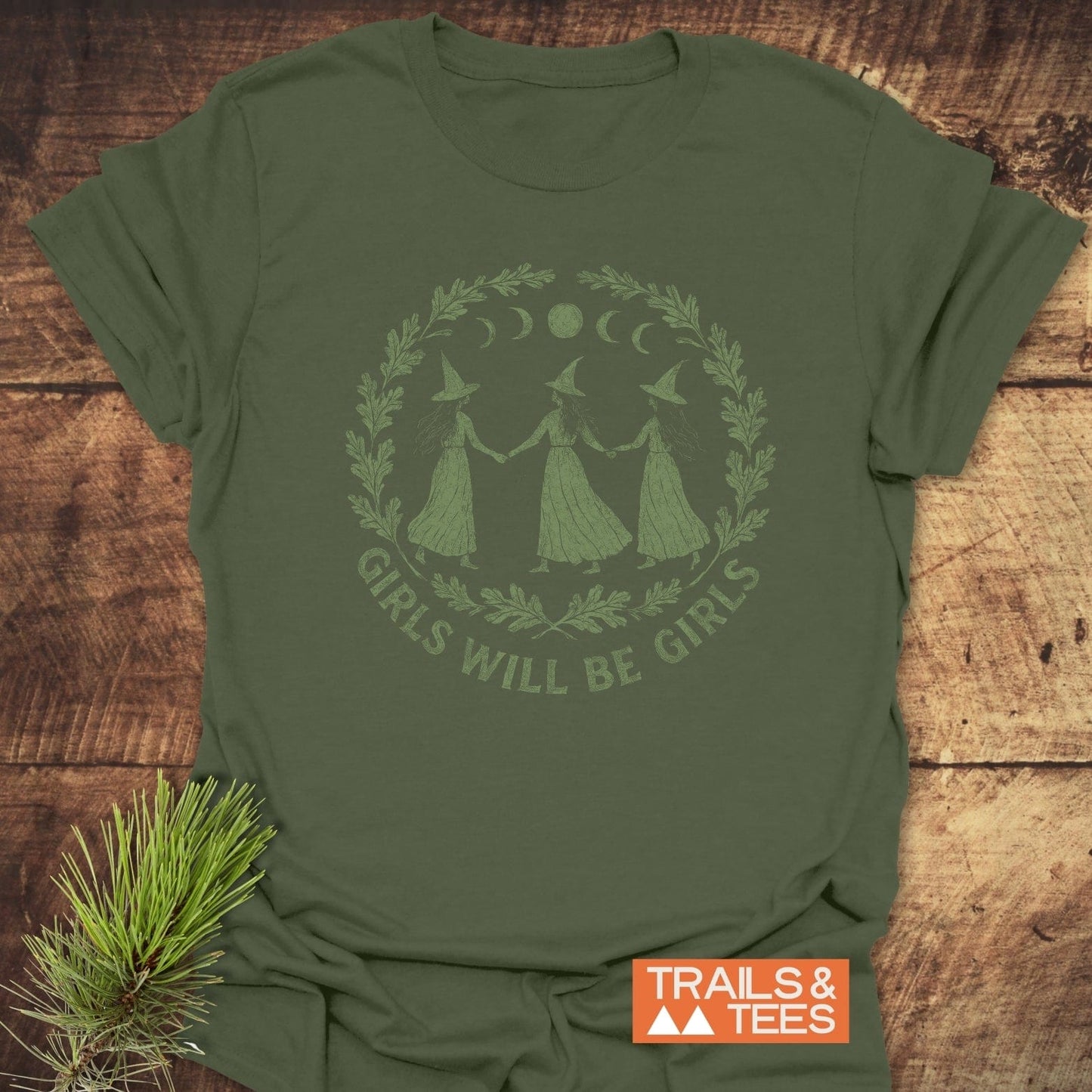 Witches Halloween T-Shirt featuring three witch figures, moon phases, and laurel wreath, slogan “GIRLS WILL BE GIRLS,” on soft, durable, ring-spun cotton.