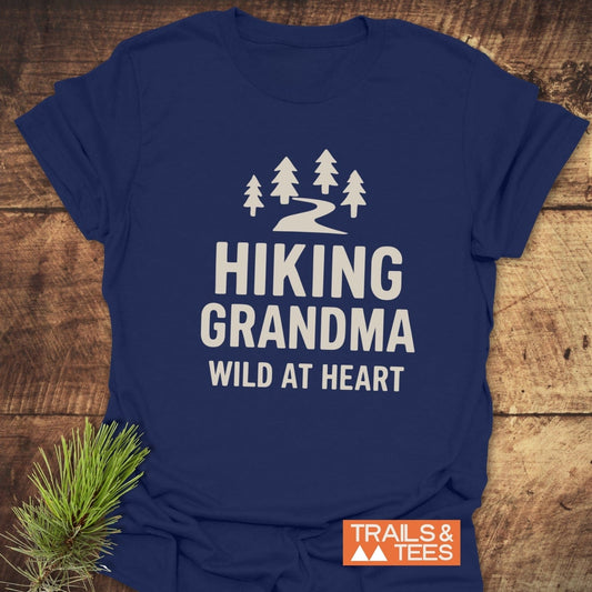 Navy-blue Hiking Grandma - Wild At Heart T-shirt with pine tree design, off-white lettering, and orange TRAILS & TEES logo, styled with pine sprig.