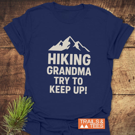 Navy-blue T-shirt with HIKING GRANDMA – TRY TO KEEP UP! in white, featuring a mountain silhouette. Includes TRAILS & TEES logo.