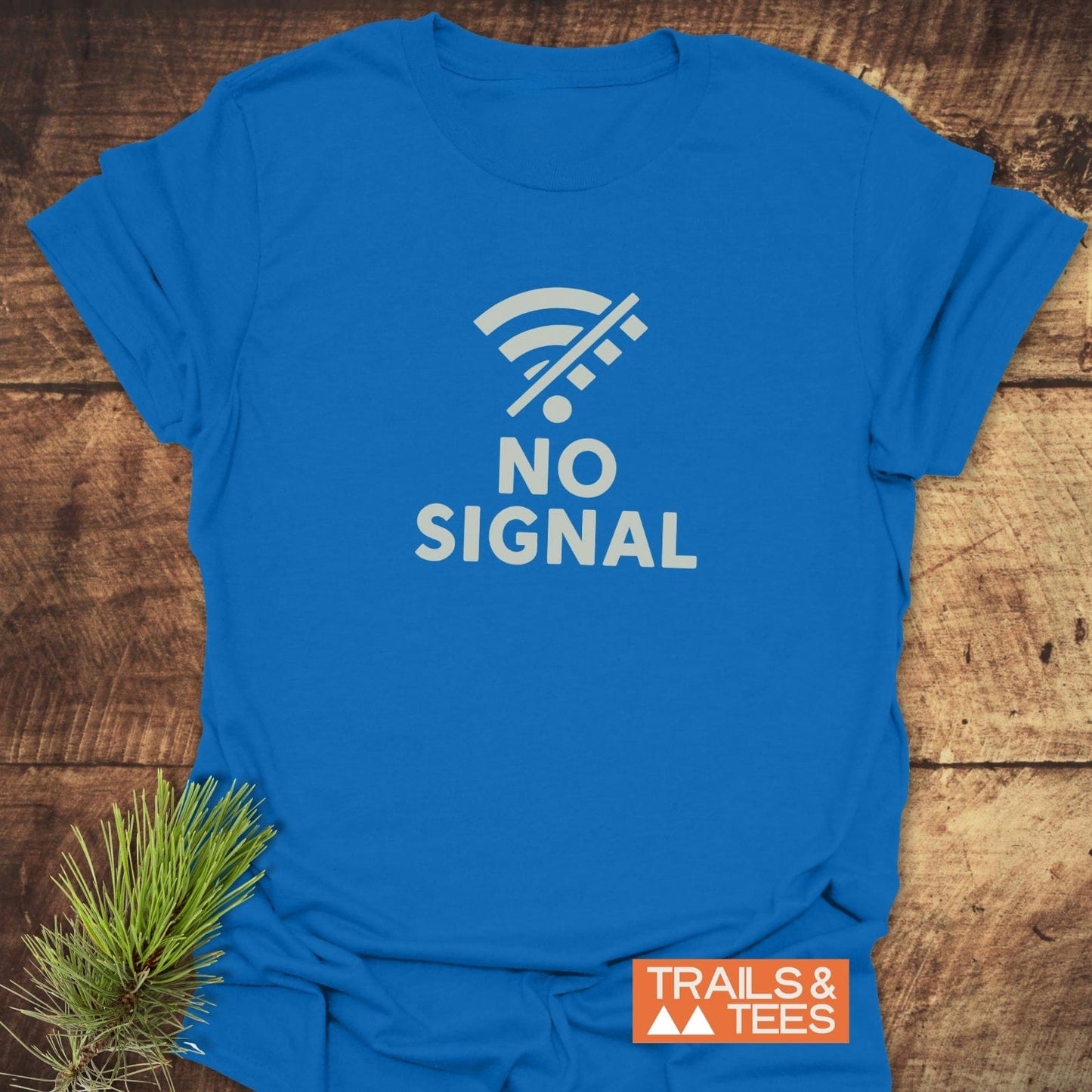 No Signal Minimalist T-Shirt featuring a white crossed-out Wi-Fi icon, laid flat with a pine sprig, showcasing Trail-tested comfort by Trails & Tees.