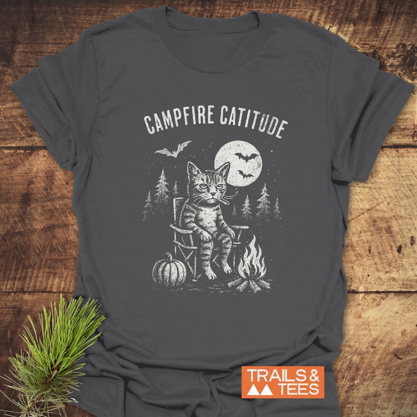 Campfire Catitude T-Shirt with grumpy cat by campfire, moonlit pine trees, and pumpkin. Soft ring-spun cotton, durable print, pre-shrunk for lasting fit.