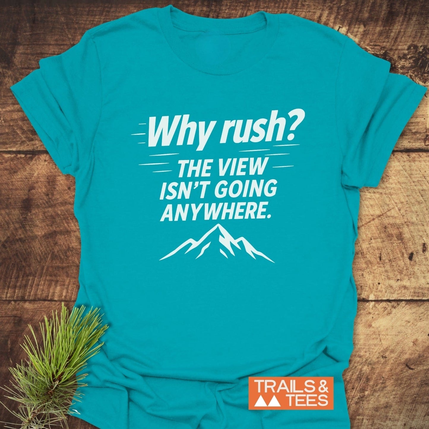 Turquoise-blue t-shirt with Why rush? The view isn’t going anywhere. slogan and mountain silhouette, highlighting Trail-tested comfort and outdoor style by TRAILS & TEES.