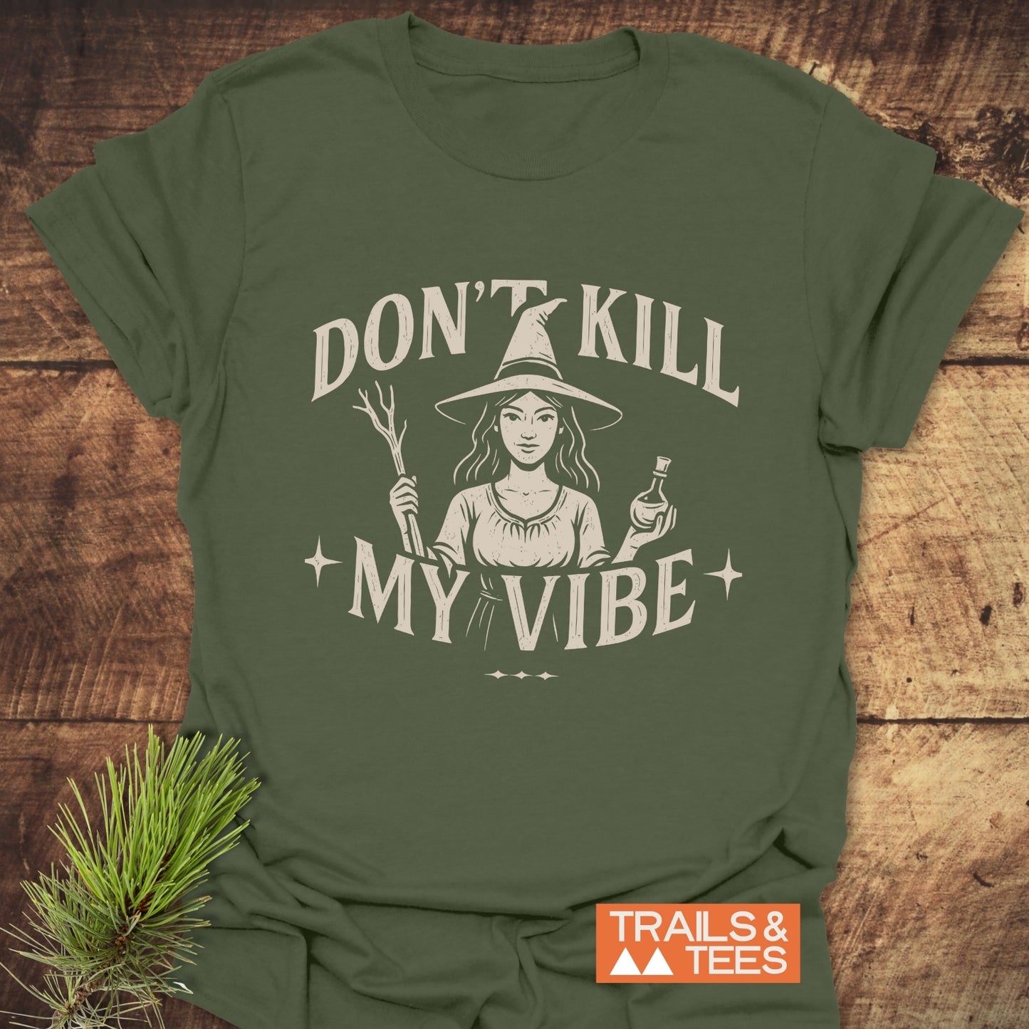 Don't Kill My Vibe Wood Witch T-Shirt features a witch graphic with a wand and potion, cream slogan, ensuring comfort and durability with pre-shrunk, ring-spun cotton.