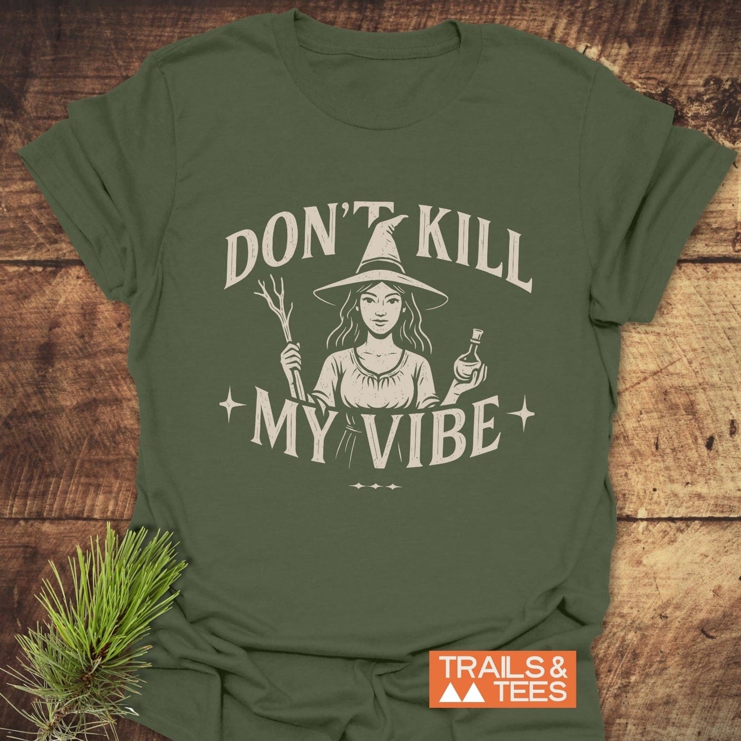 Don't Kill My Vibe Wood Witch T-Shirt features a witch graphic with a wand and potion, cream slogan, ensuring comfort and durability with pre-shrunk, ring-spun cotton.