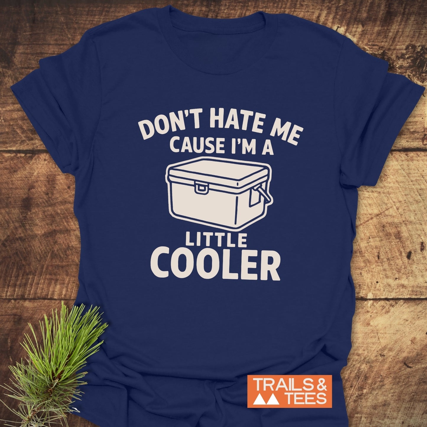 Navy-blue A Little Cooler Camping T-Shirt with a cooler illustration, crafted from soft cotton for outdoor comfort and durability, displayed on a wooden surface.