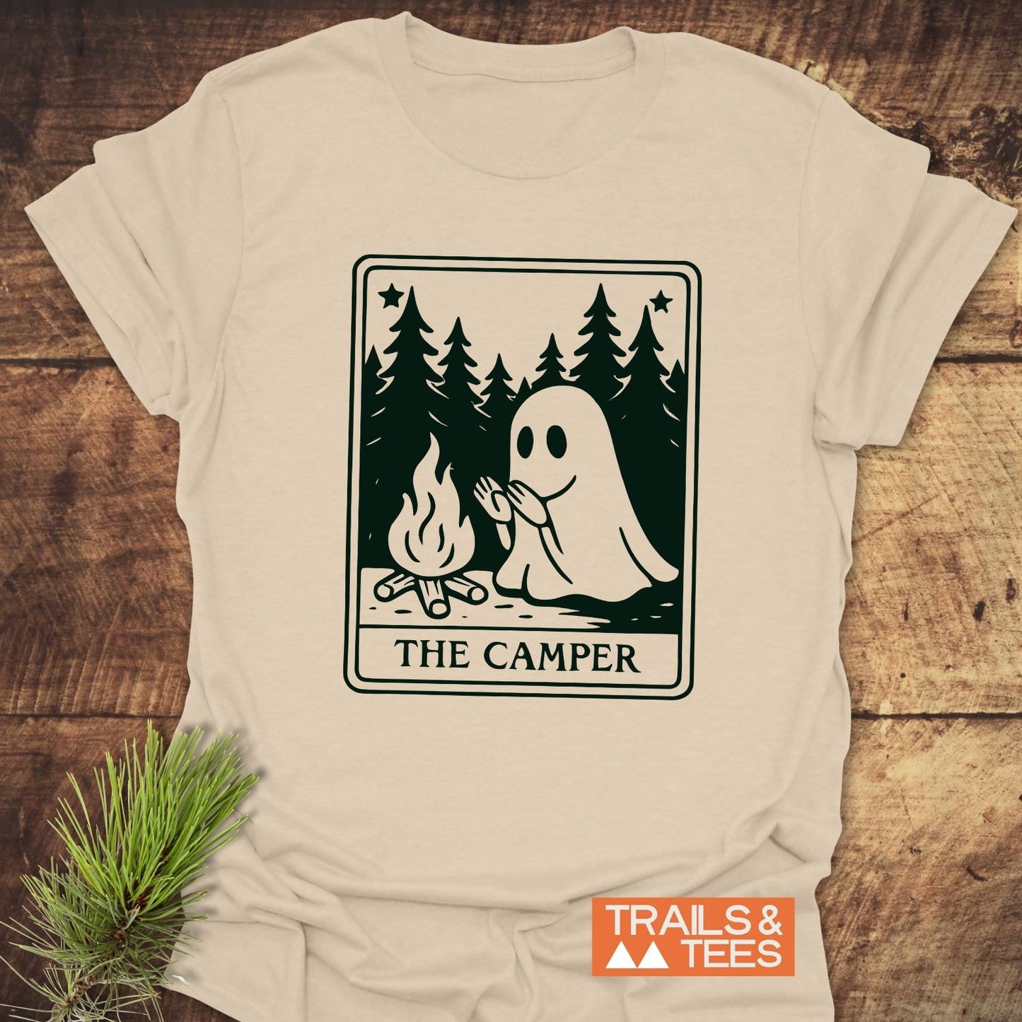 The Camper Retro Tarot T-Shirt features a ghost by a campfire in a pine forest, crafted from soft cotton for comfort and durability.