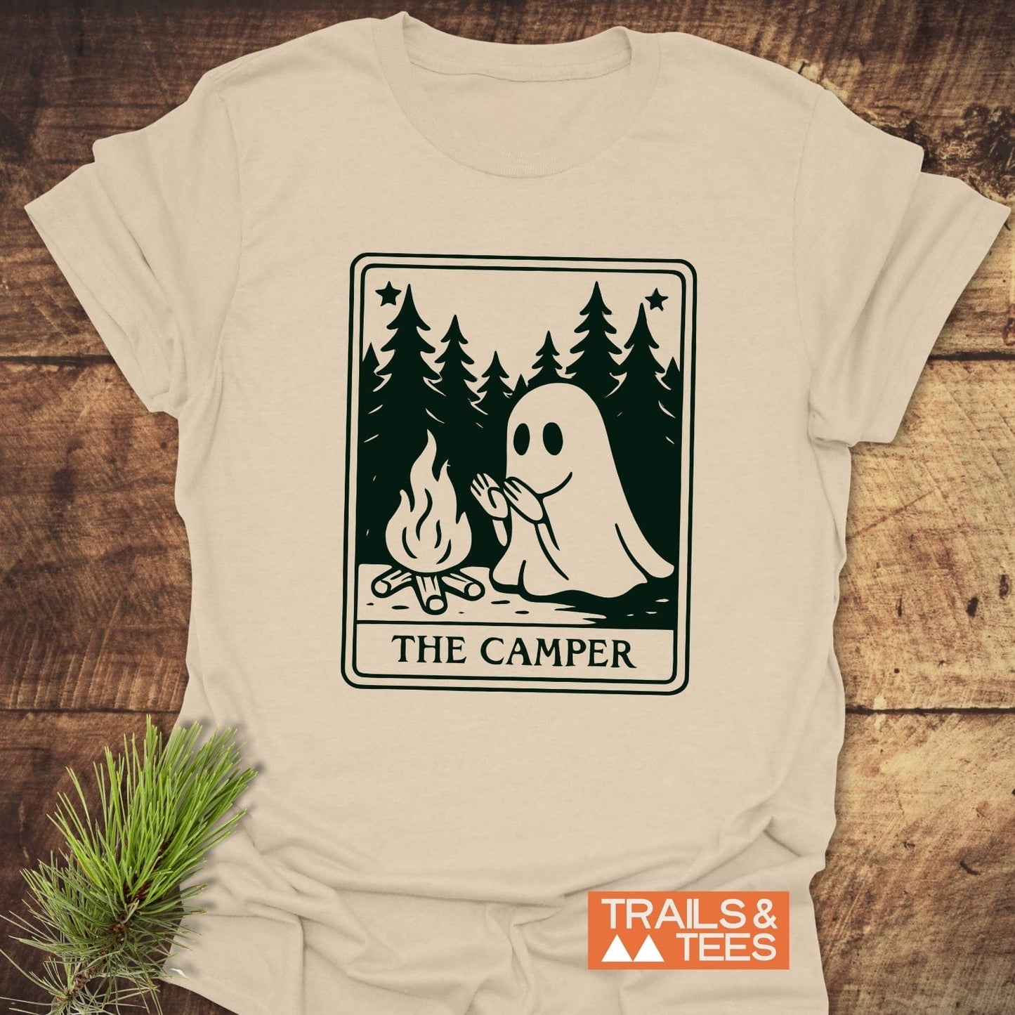 The Camper Retro Tarot T-Shirt features a ghost by a campfire in a pine forest, crafted from soft cotton for comfort and durability.