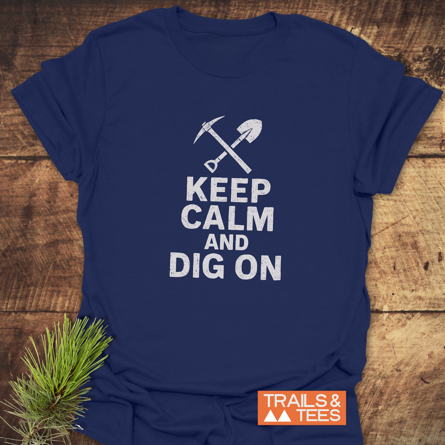 Navy-blue Keep Calm Rock Lover T-Shirt with white pickaxe and shovel graphic, slogan, and orange TRAILS & TEES logo, showcasing outdoor adventure spirit.
