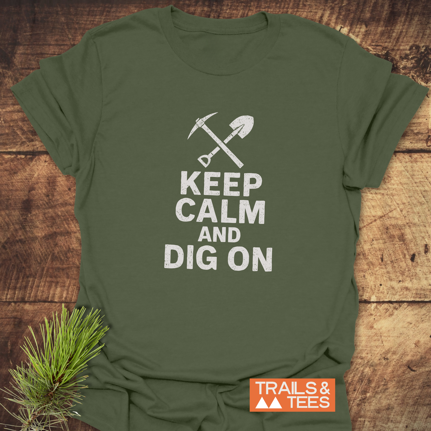 Keep Calm Rock Lover T-Shirt with white pickaxe and shovel design, slogan KEEP CALM AND DIG ON, on soft, durable cotton. Trails & Tees logo visible.