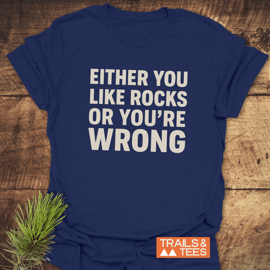 Navy “Either You Like Rocks T-Shirt” on wooden surface, featuring white block text and Trails & Tees logo, highlighting outdoor adventure and comfort.