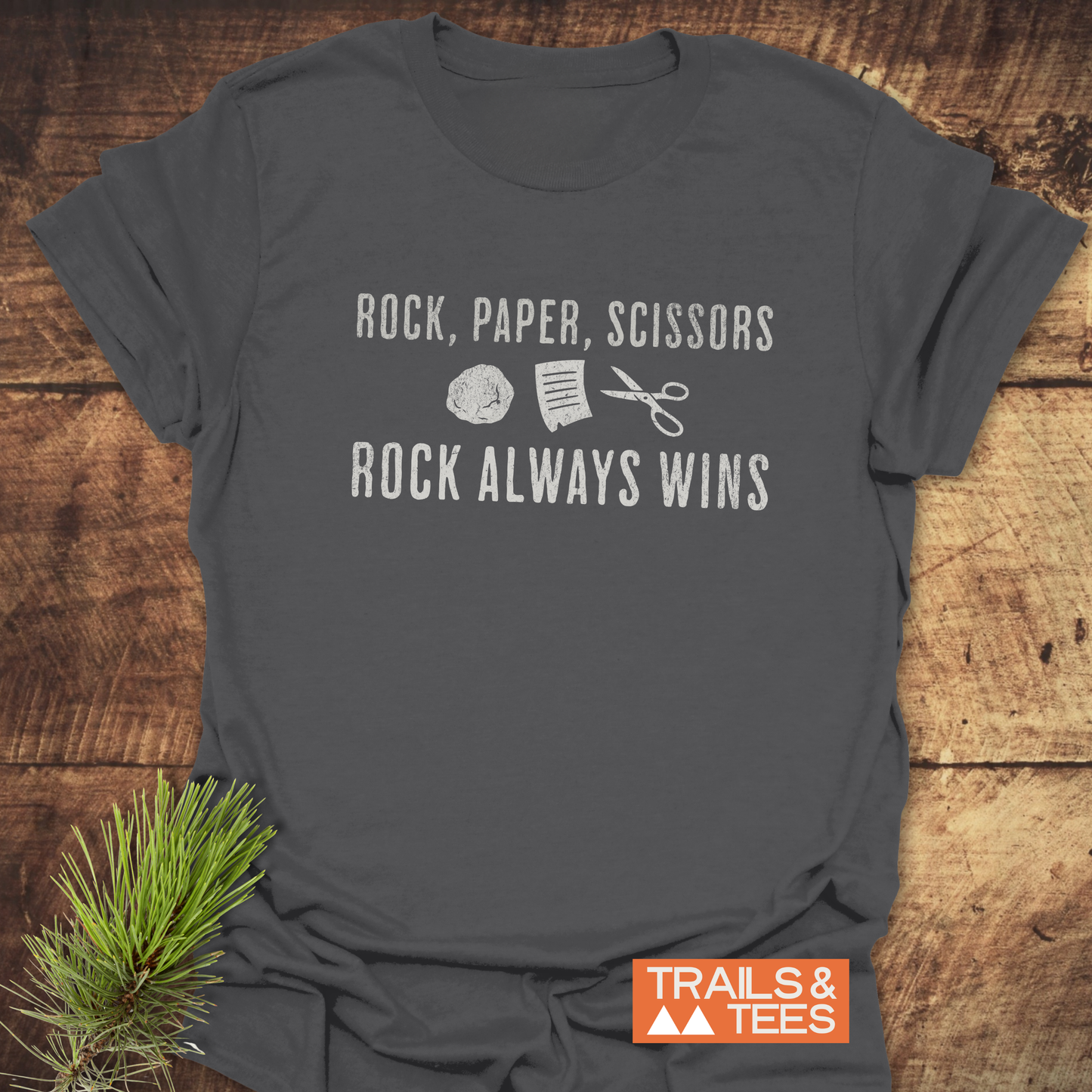 Heather-gray Rock Paper Scissors T-Shirt on wood surface, featuring graphic and slogan, with Trails & Tees logo, showcasing trail-tested comfort and durable design.