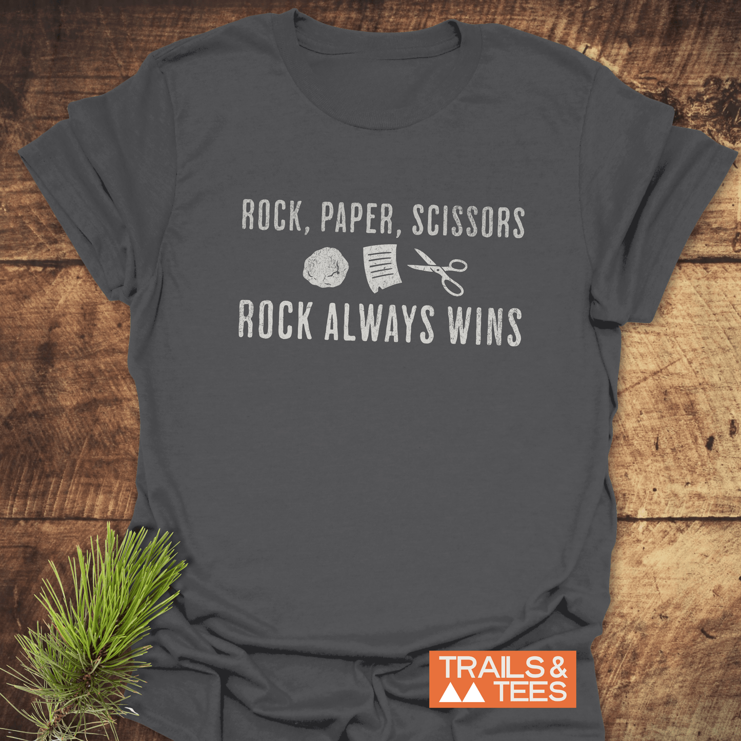 Heather-gray Rock Paper Scissors T-Shirt on wood surface, featuring graphic and slogan, with Trails & Tees logo, showcasing trail-tested comfort and durable design.