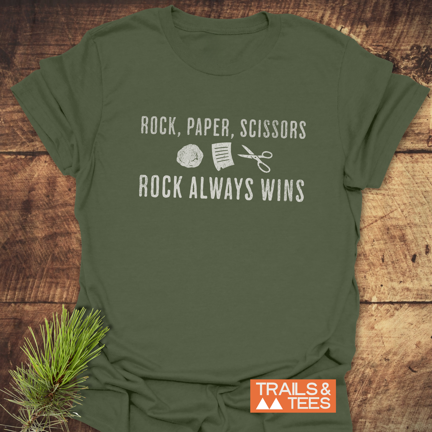 Rock Paper Scissors T-Shirt featuring a white graphic and playful text, laid on wood. Made from soft, ring-spun cotton with durable print.