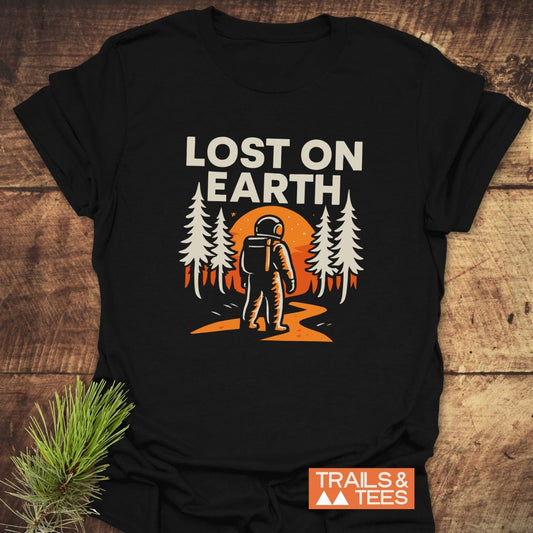 Lost On Earth T-Shirt featuring an astronaut graphic amidst pine trees and an orange sun, highlighting outdoor adventures, crafted from soft, lightweight cotton for comfort.