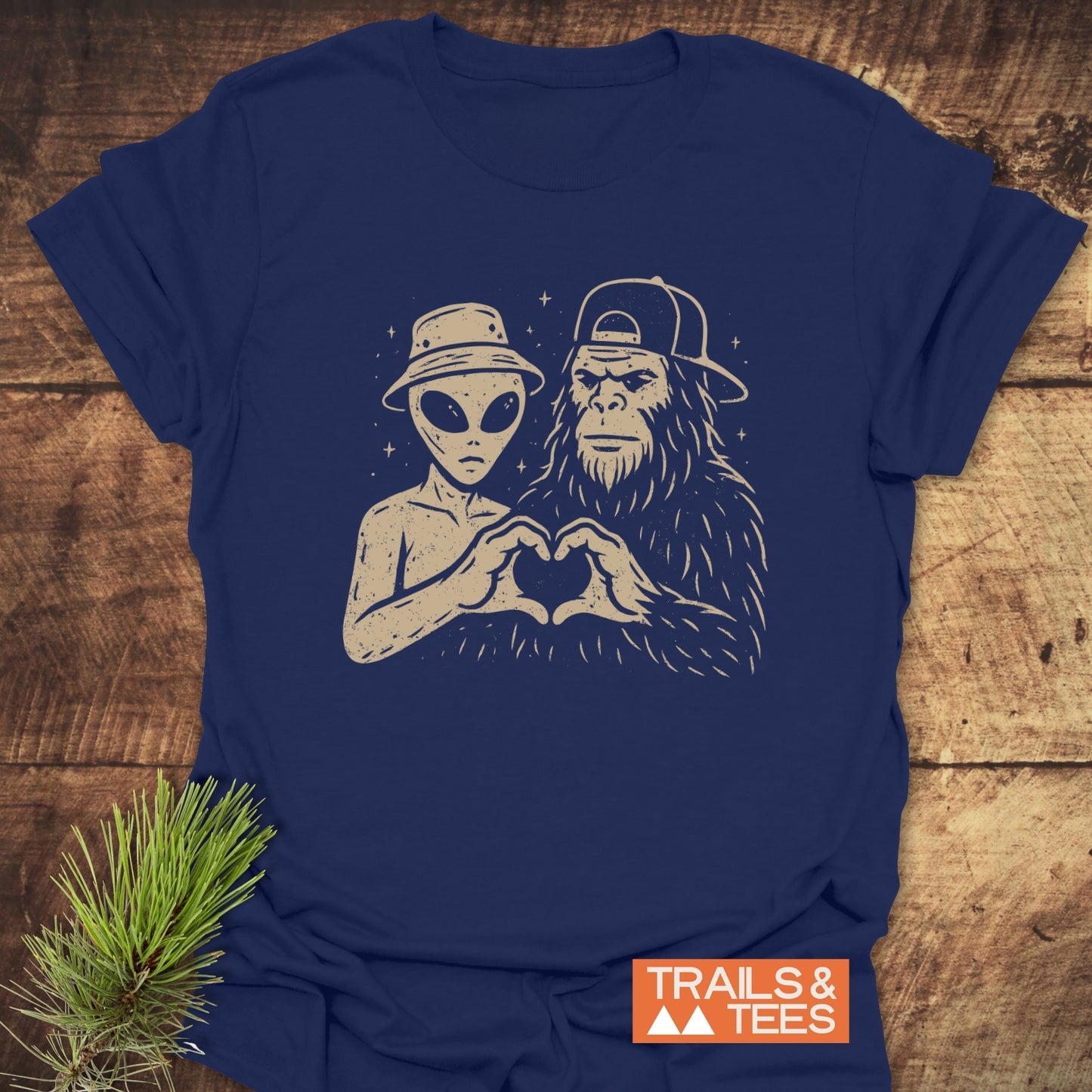 Strange Love Bigfoot T-Shirt featuring an alien and Bigfoot forming a heart, printed on navy-blue cotton. Durable, lightweight, pre-shrunk, ideal for outdoor adventures.