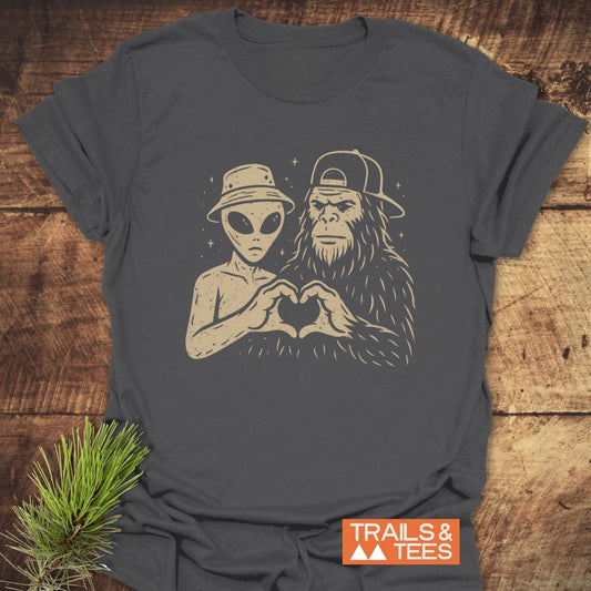 Strange Love Bigfoot T-Shirt featuring an alien and Bigfoot forming a heart. Crafted from soft cotton, this tee offers comfort for everyday adventures.