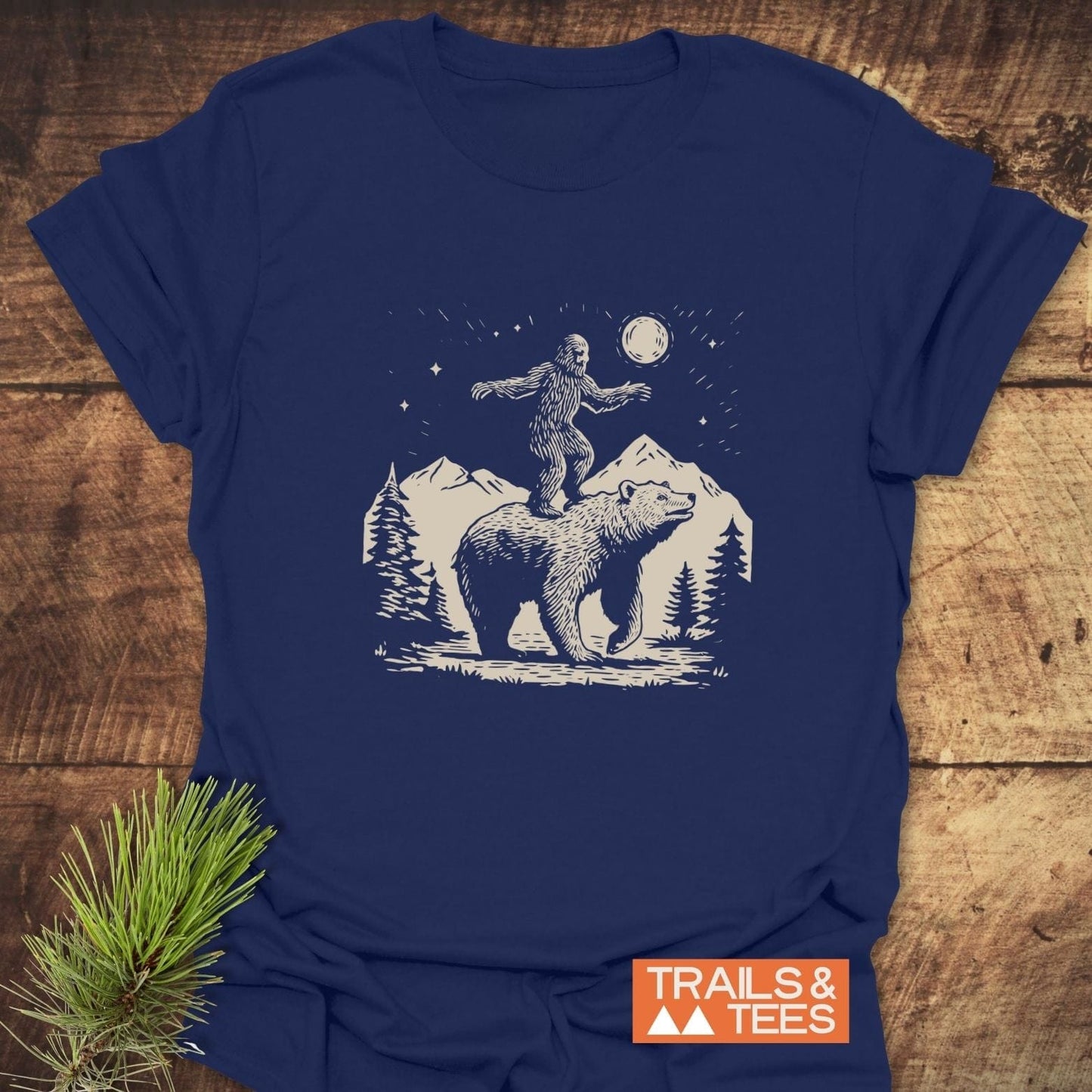 Bigfoot And Bear Funny T-Shirt featuring a bear in mountain scene with sasquatch. Trail-tested comfort, lightweight cotton, pre-shrunk, and durable print.