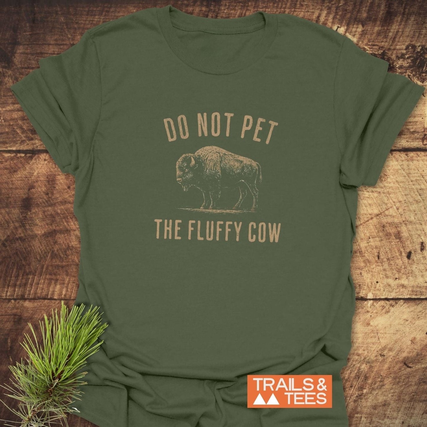 Do Not Pet Bison T-Shirt features a vintage bison drawing with text, laid on wood with pine sprig, branded TRAILS & TEES logo visible.